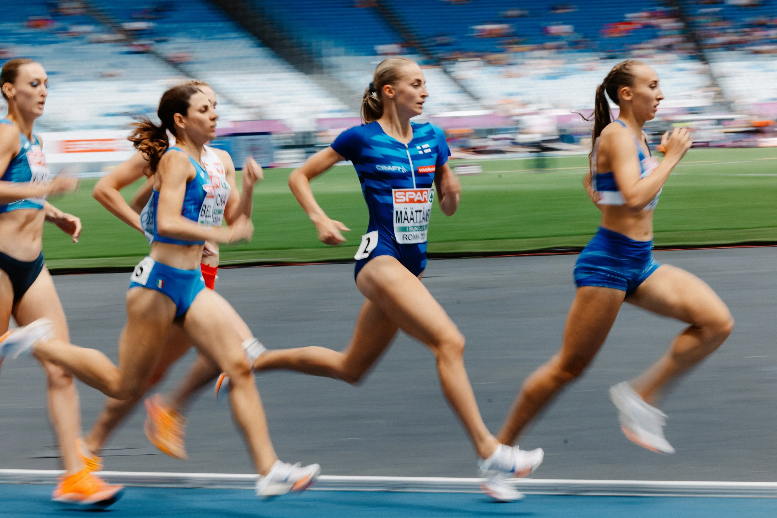 Juoksijoita Suomen kilpailuasuissa stadionin radalla.
